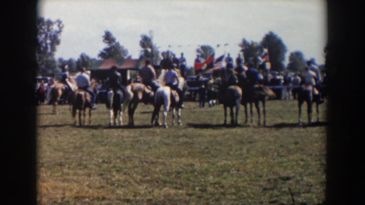 Seven horseback riders line up in a sunny Wheeling, Ohio field in 1957, with spectators, flags, and trees behind them.