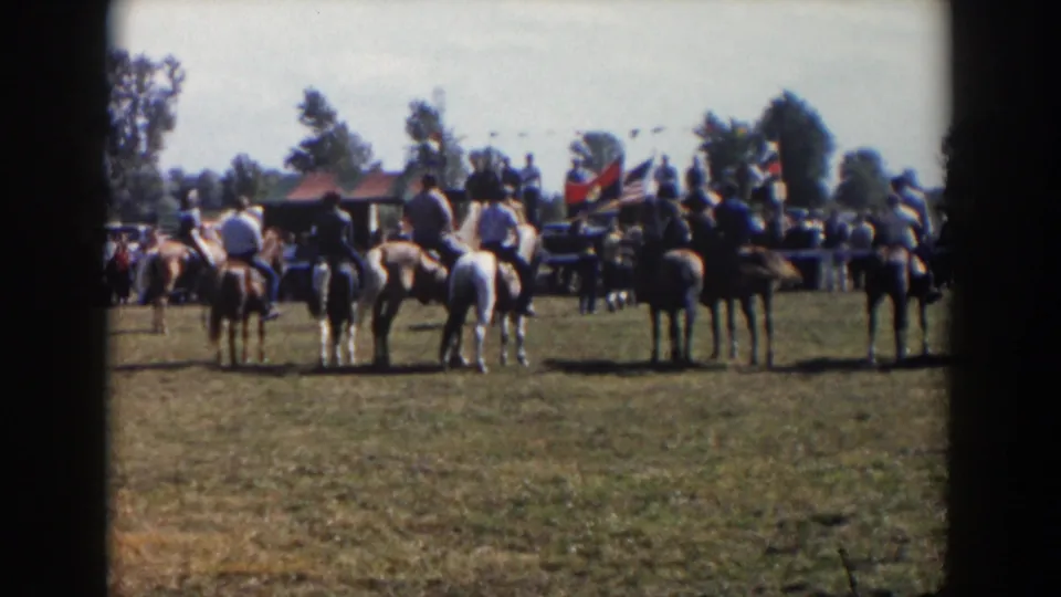 Seven horseback riders line up in a sunny Wheeling, Ohio field in 1957, with spectators, flags, and trees behind them.
