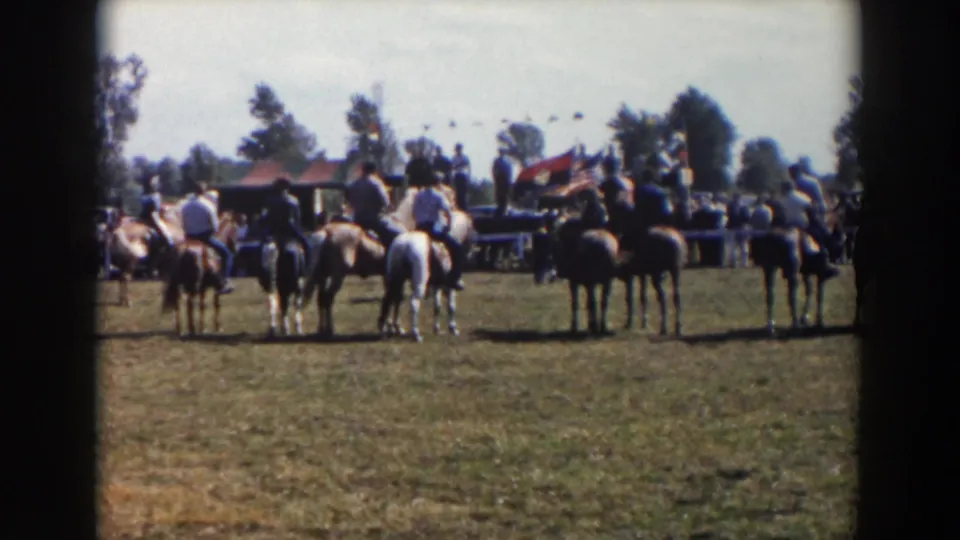 A line of horseback riders remains in place at a 1957 Wheeling, Ohio outdoor gathering, viewed from behind across the field.