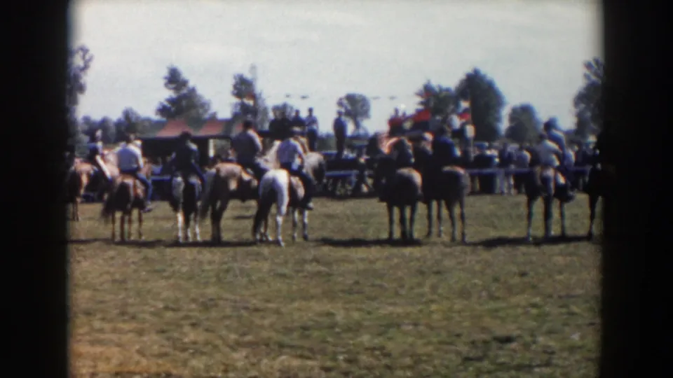 A 1957 8mm frame from Wheeling, Ohio shows the horseback lineup spread across the field with flags and spectators behind.