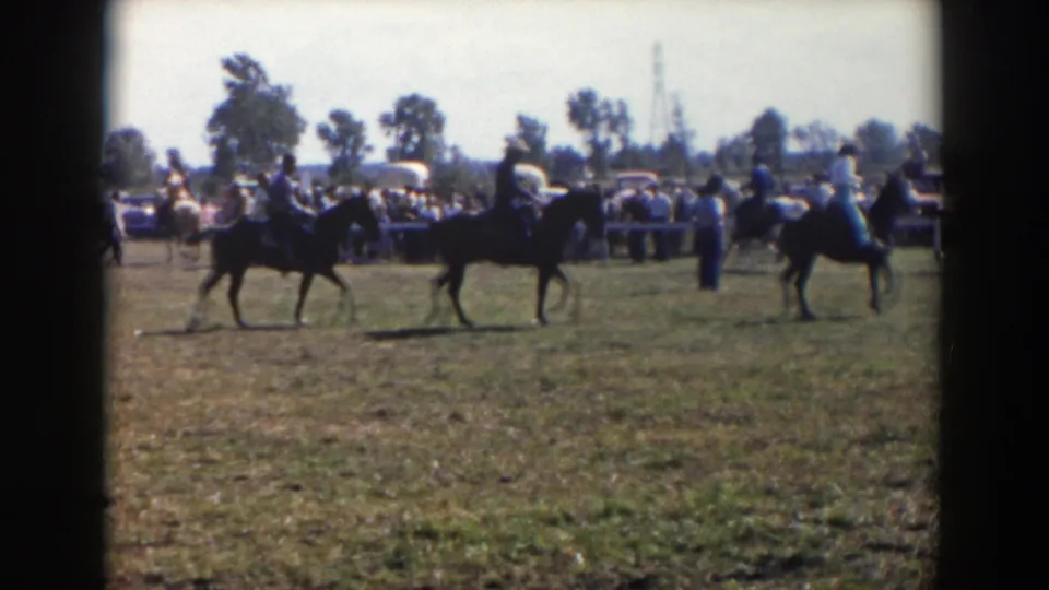 Three riders on horseback move apart across the grassy field as a distant crowd watches the 1957 Wheeling, Ohio riding event.