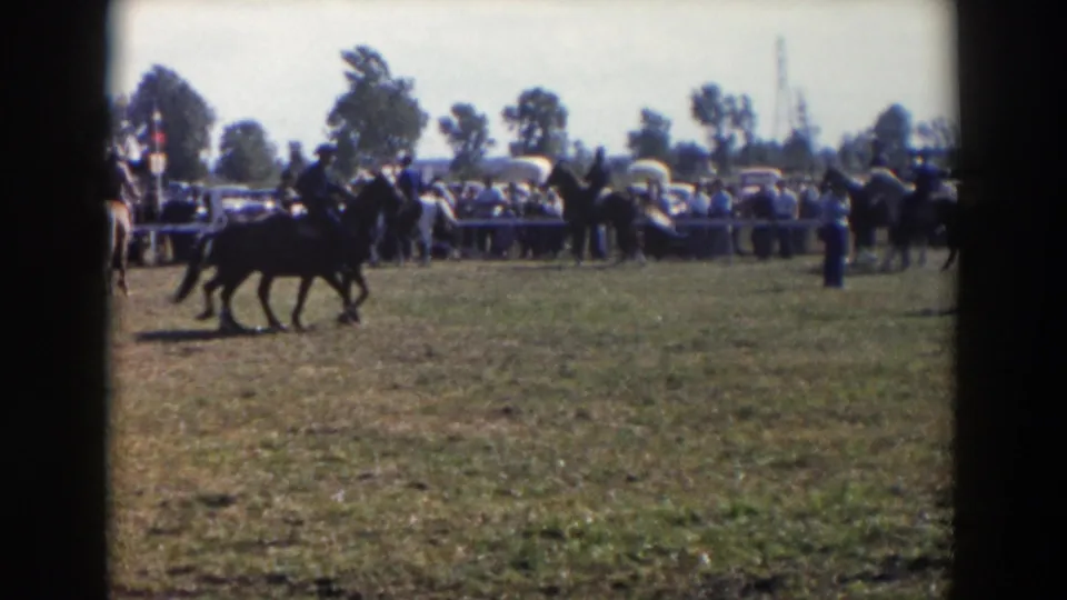 Wheeling, Ohio horse show frame with two mounted riders crossing a grassy field before a distant fair crowd.