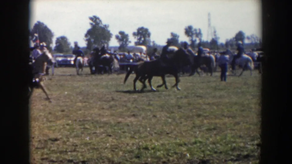 Riders and horses appear in formation on a Wheeling, Ohio field, with a line of spectators and classic cars behind them.