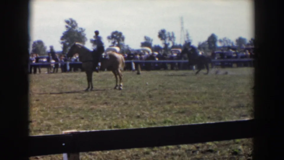 A saddled horse and rider appear in the grassy Wheeling, Ohio enclosure, with more riders and spectators near the rail in the background.