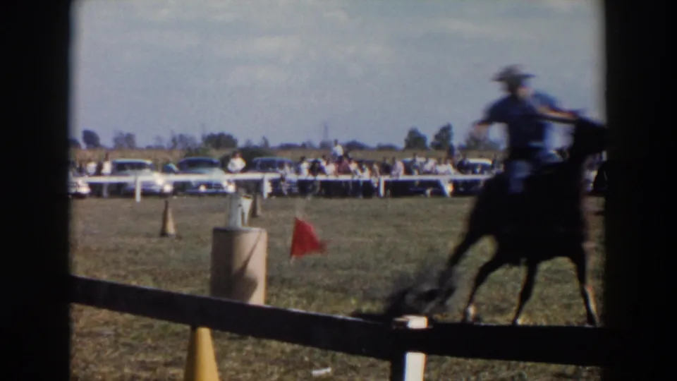 The rider passes near the camera in blurred motion beside a red marker flag on a grassy Wheeling fairground course.