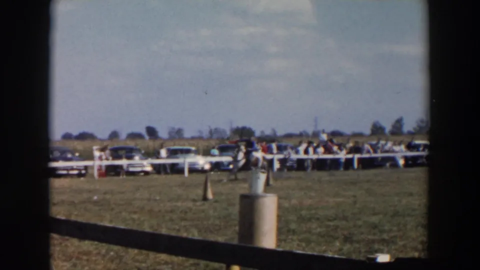 Near the end of the clip, the mounted rider moves away across the fairground course with the spectator line and midcentury cars behind.