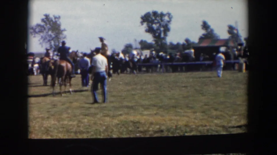 Two riders on horseback and a standing figure appear on the Wheeling, Ohio field as the crowd watches the equestrian event.