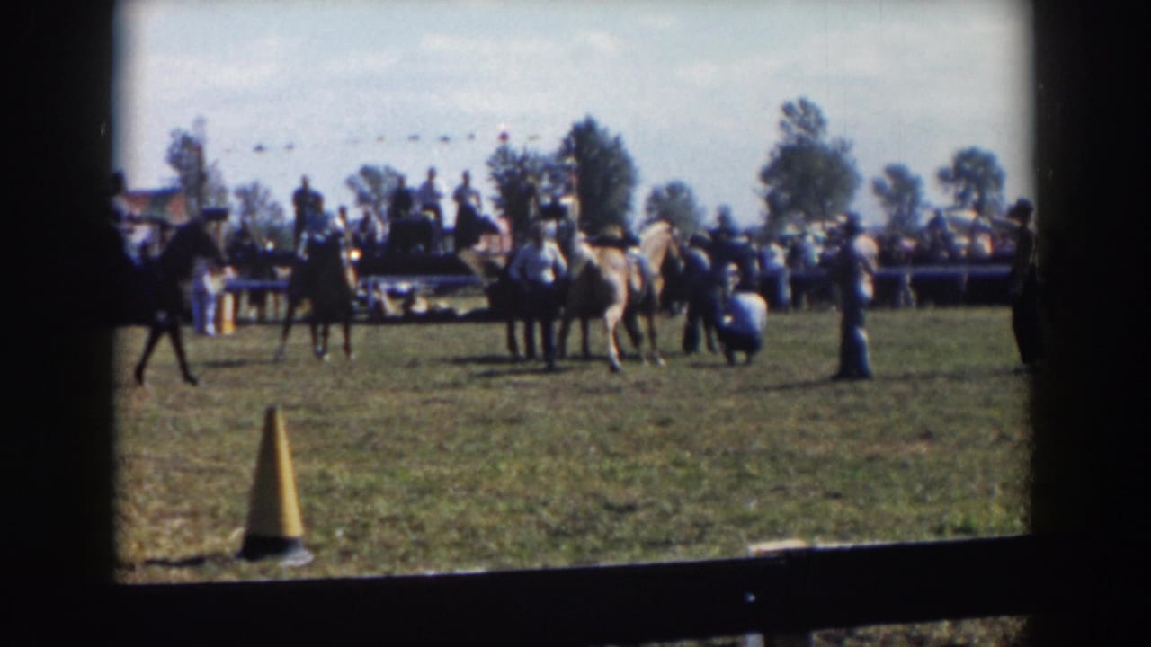 A rider passes at left while other riders and spectators stand near the center of the field.