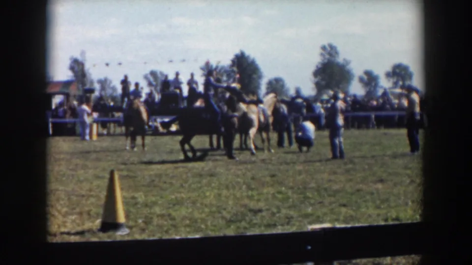 1957 Wheeling, Ohio home-movie frame showing a horse crossing the field near riders, spectators, parked cars, and overhead bunting.