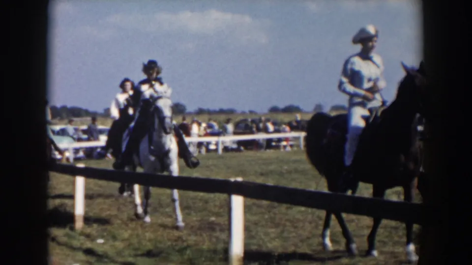 Closer 1957 8mm view of riders in Western attire passing near the fence at a small Wheeling, Ohio horse event.