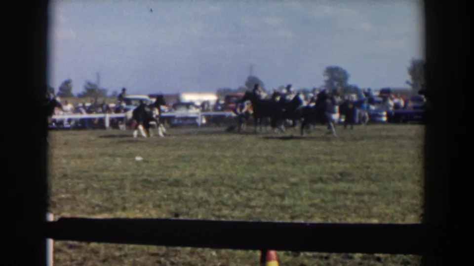 Horses with saddle riders continue through the Wheeling, Ohio enclosure, framed by dark 8mm borders and a foreground fence.