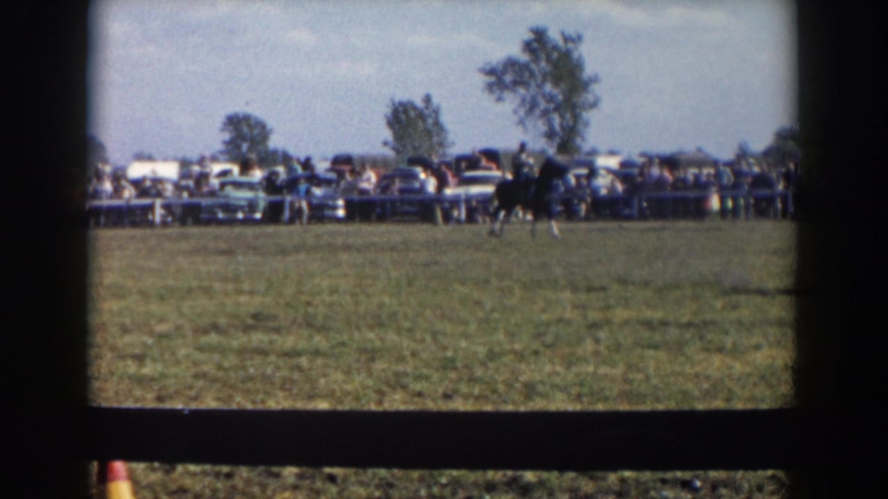 A horse and rider cross the grass at a rural fair in the supplied Wheeling, Ohio 1957 home-movie footage, with spectators lining the edge.