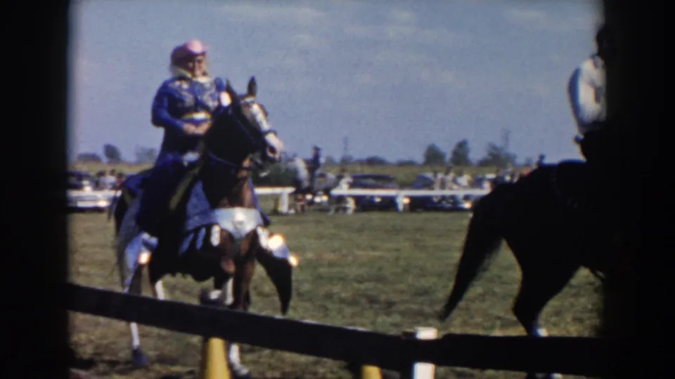 A rider in blue clothing sits on a decorated horse as another horse crosses the foreground during the 1957 Wheeling, Ohio event.
