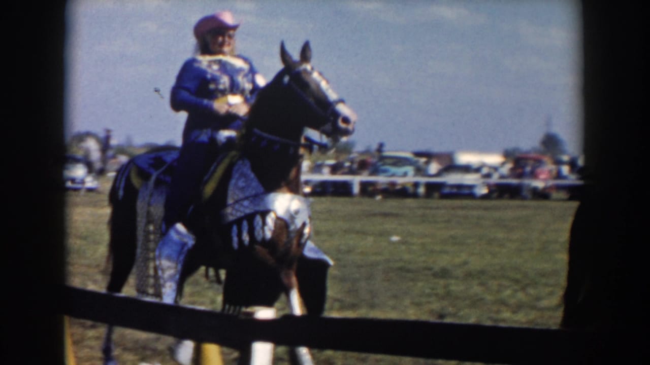 1957 home-movie frame identified as Wheeling, Ohio, showing a rider in blue on a decorated dark horse at a field event.
