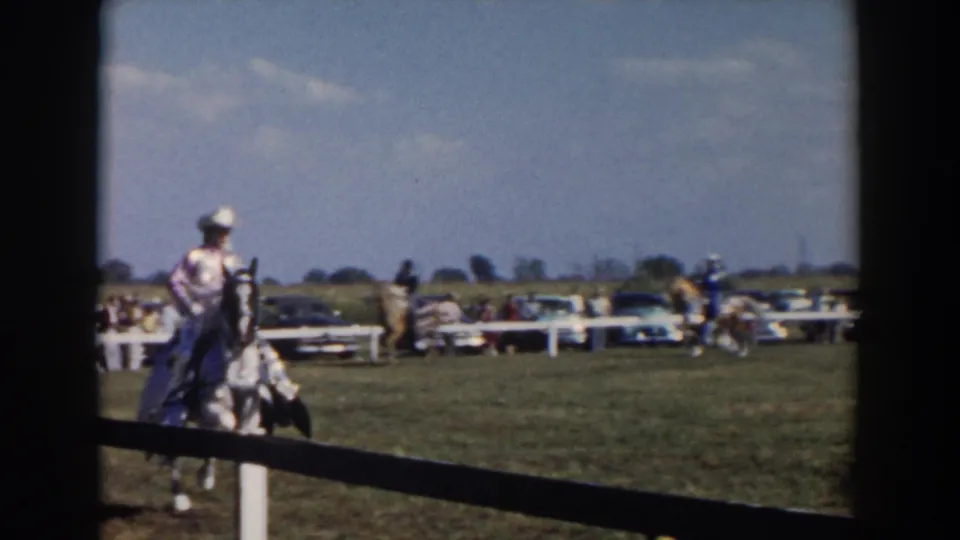 1957 Wheeling, Ohio 8mm frame of a rider in western-style clothing guiding a horse across a grassy event field.