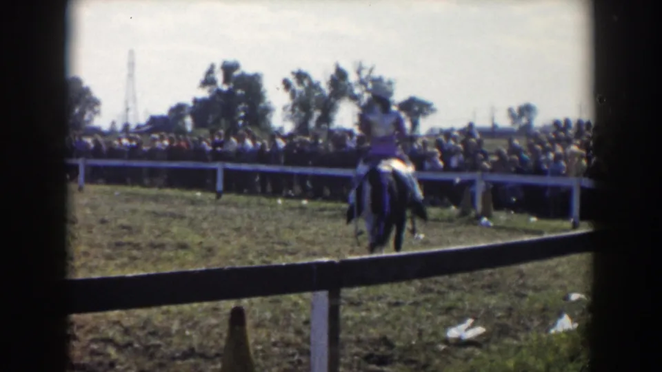1957 Wheeling, Ohio home-movie frame showing a rider on horseback near a white show-ring barrier with a crowd in the background.
