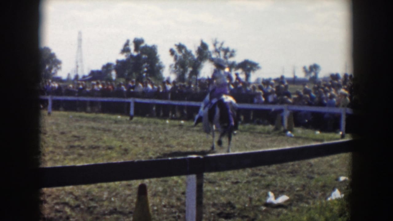 Horse and rider continue around the ring with a dense crowd beyond the white fence.