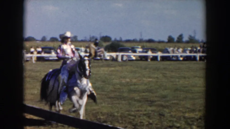 A rider on a light horse moves through the Wheeling, Ohio show ring in 1957, with spectators, fencing, and parked cars behind.