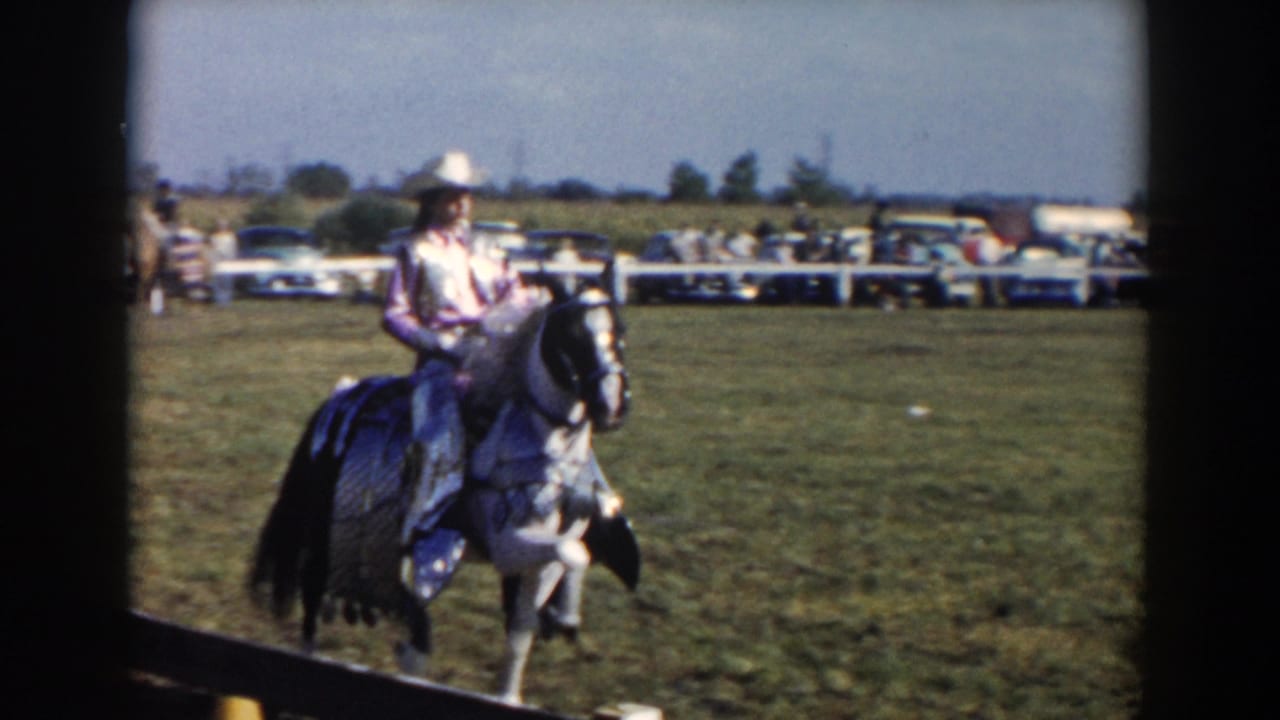 Woman in a white cowboy hat rides a black and white horse across a grassy show ring.