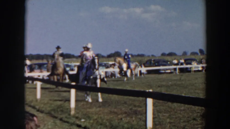 A pair of mounted riders, one in a dark hat and one in lighter clothing, pass through the 1957 Wheeling, Ohio event scene.
