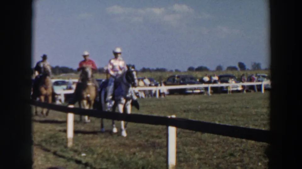 Mounted riders at the Wheeling, Ohio equestrian event approach the foreground, framed by a white fence and dark film border.