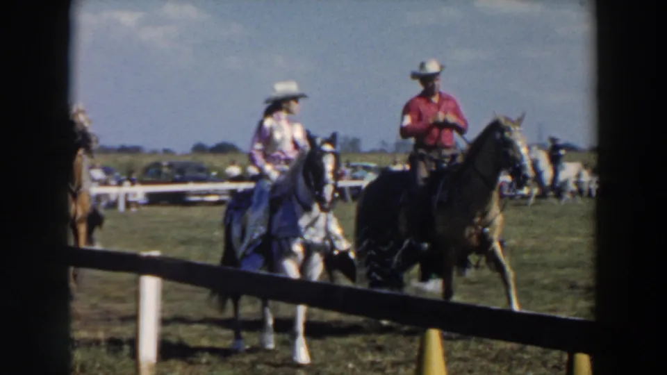 A man in a red shirt and another white-hatted rider appear on horseback at a 1957 Wheeling, Ohio field event.