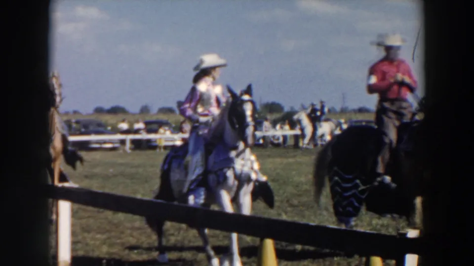 1957 8mm home-movie frame from Wheeling, Ohio showing riders on horses in a grassy arena behind a fence.