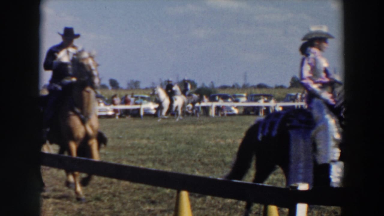 Three riders on horses pass through a fenced outdoor arena with spectators beyond.