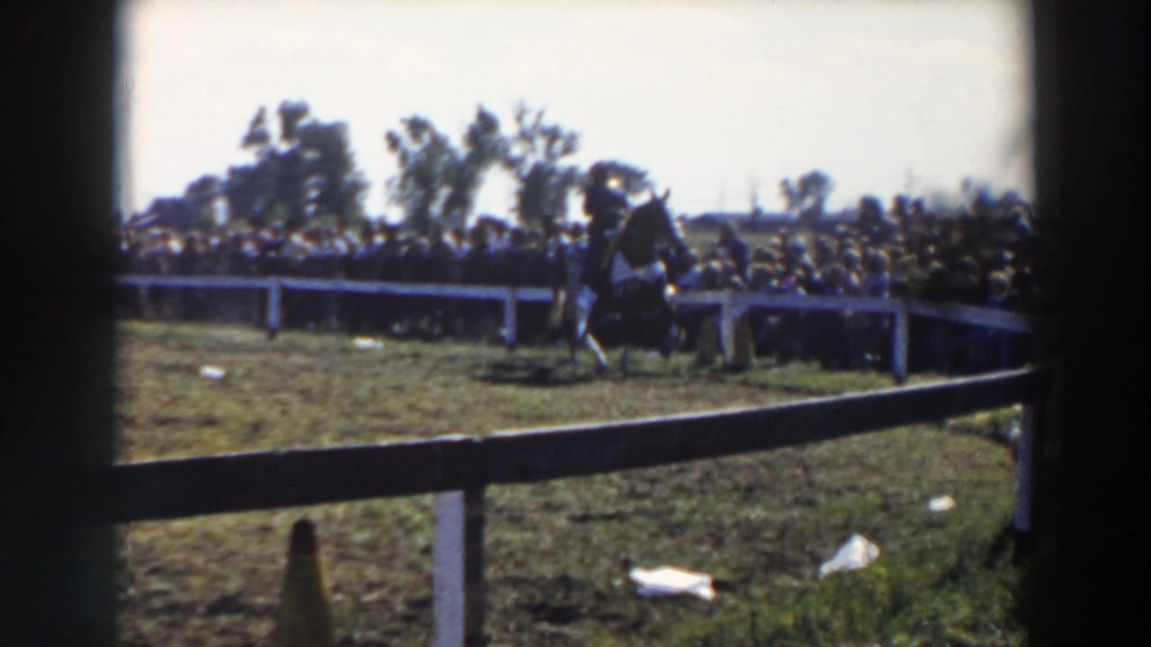 1957 Wheeling, Ohio home-movie frame of a rider on horseback circling a grassy pen before a large crowd.
