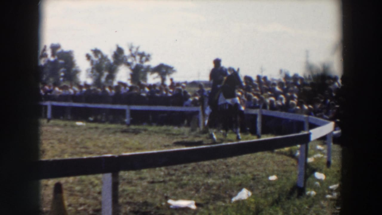 Mounted rider continues around the fenced pen with spectators filling the background.