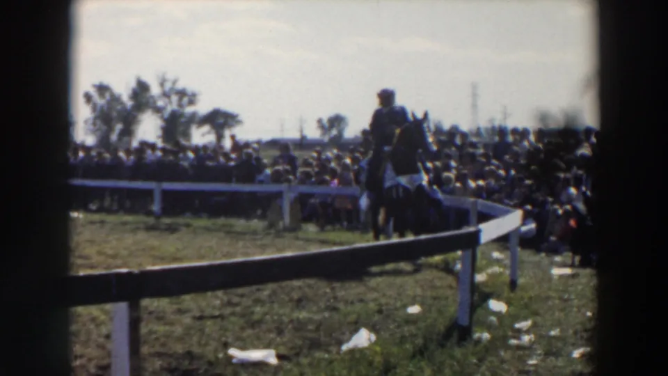 1957 home-movie view of a horse rider rounding a grassy pen in Wheeling, Ohio, with spectators behind the rail.