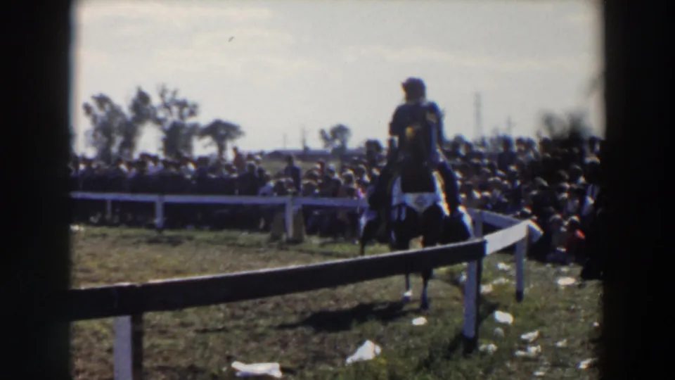 Close 8mm frame of the Wheeling, Ohio horse rider passing the fence during a 1957 outdoor fair scene.