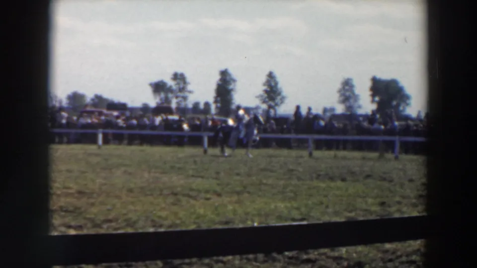 The closing frame shows the fenced horse track from a distance, with spectators, cars, trees, and the rider near the rail.