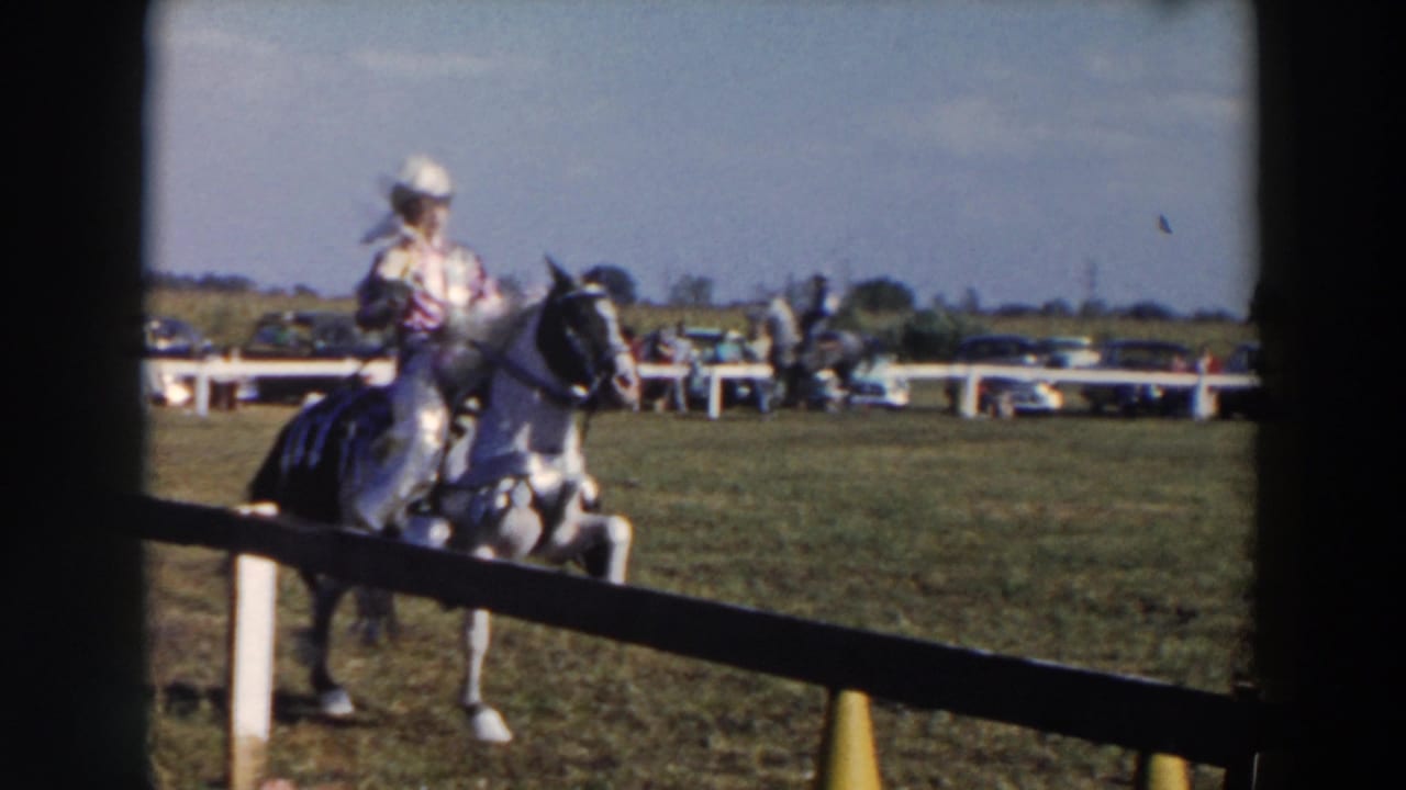 Rider in a cowboy hat on a light horse near a white fence and grassy field.