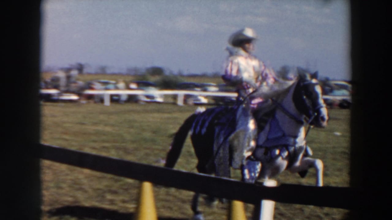 Rider in patterned clothing on a light horse moving beside the show-ring fence.