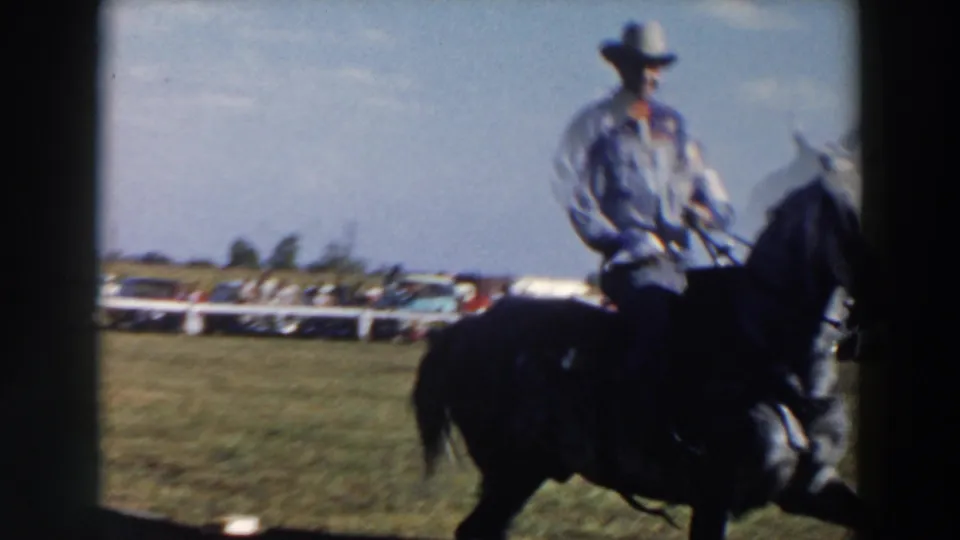 The rider on a dark horse passes close to the camera, partially framed by the fence, at the Wheeling horse event.