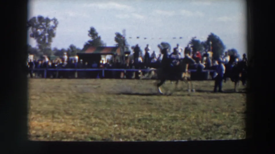 Multiple riders appear on the grassy course as spectators watch from behind a barrier in 1957 Wheeling, Ohio home-movie footage.