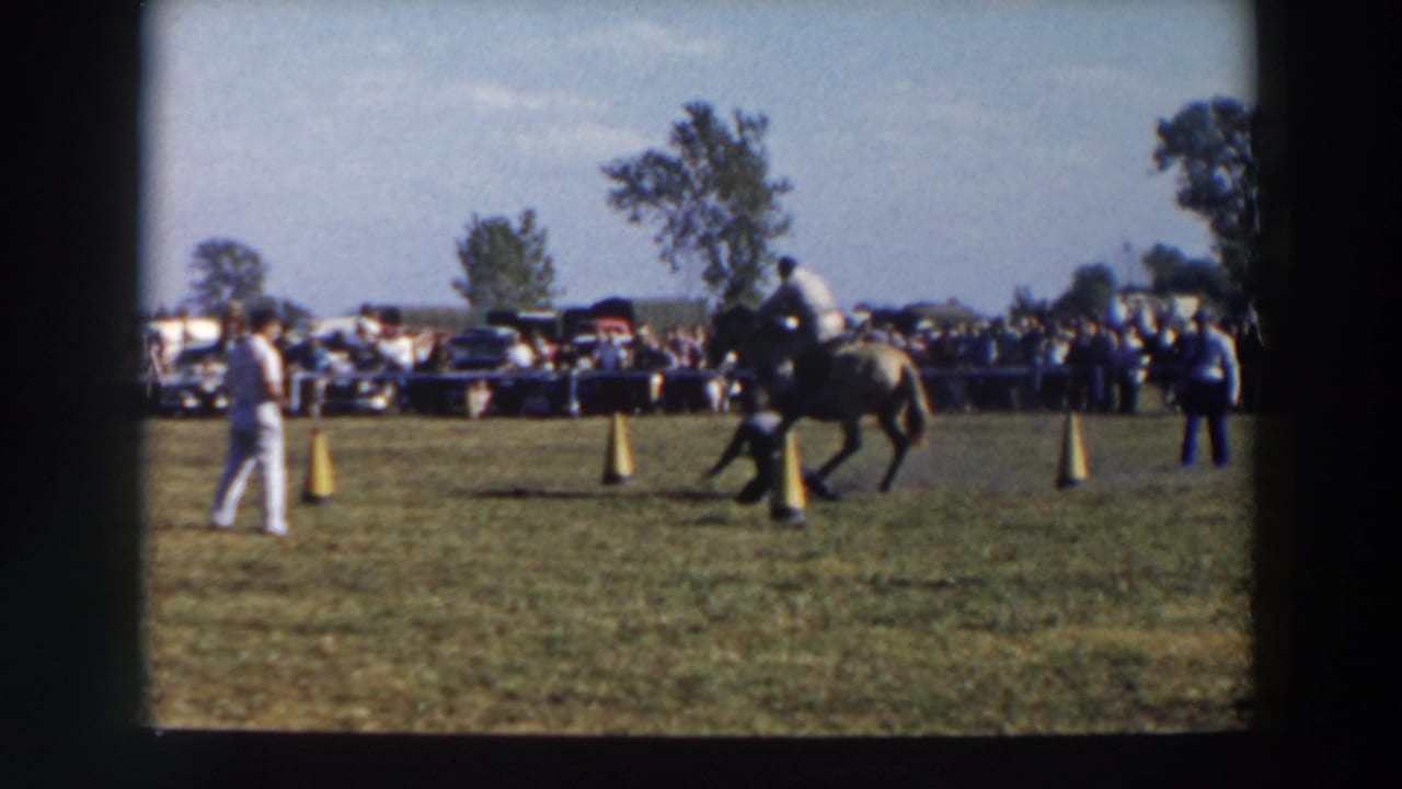 A mounted rider moves through yellow cones on a grassy course in Wheeling, Ohio, with spectators and parked cars in the background.