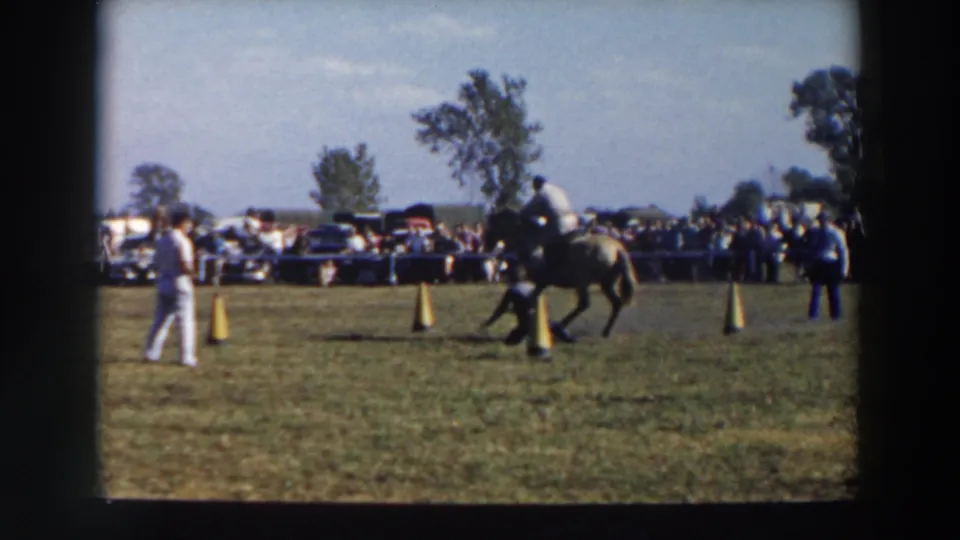 A mounted rider moves through yellow cones on a grassy course in Wheeling, Ohio, with spectators and parked cars in the background.