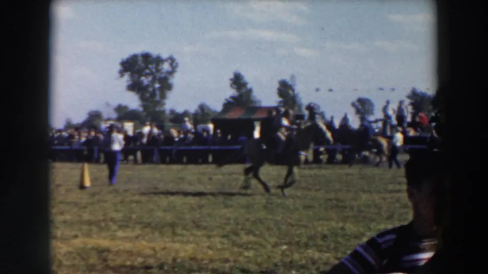 A horse and rider pass through the course in a 1957 Wheeling, Ohio home movie, with spectators, trees, and a foreground figure at frame edge.
