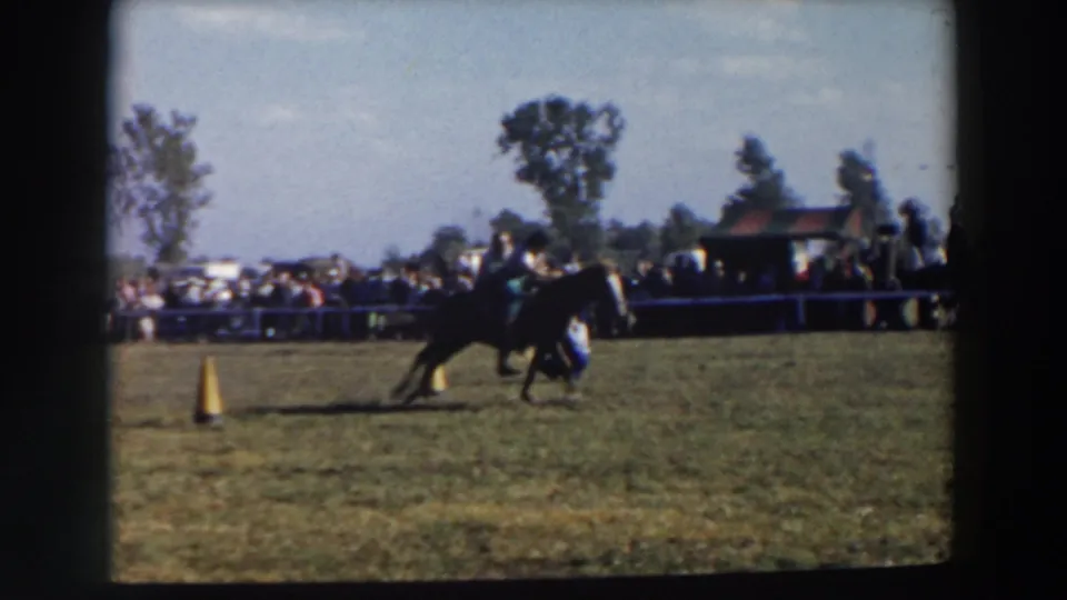 In 1957 Wheeling, Ohio footage, a rider guides a horse near a cone during an outdoor horse competition while spectators watch from the field edge.