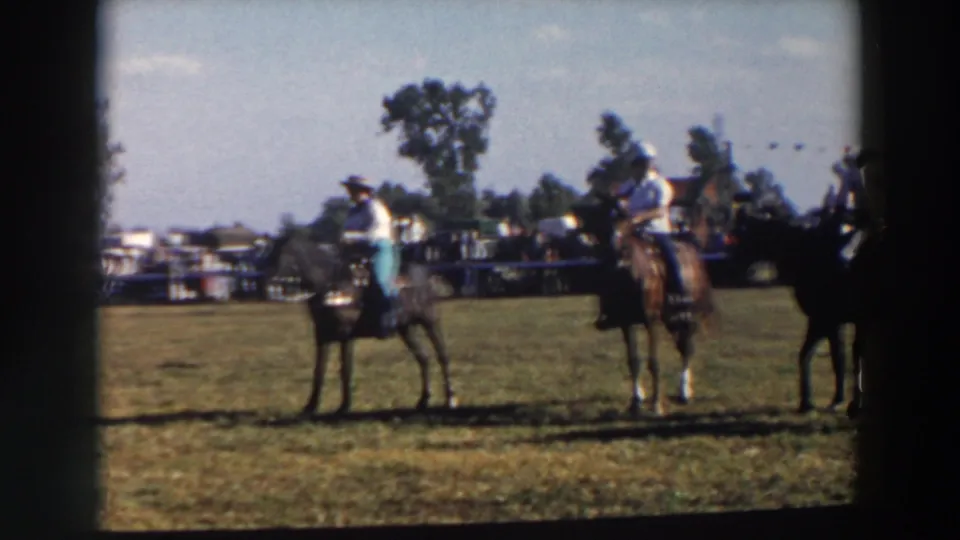 Mounted riders pause across the outdoor course in Wheeling, Ohio, with a crowd, trees, and open grass visible in the 8mm frame.