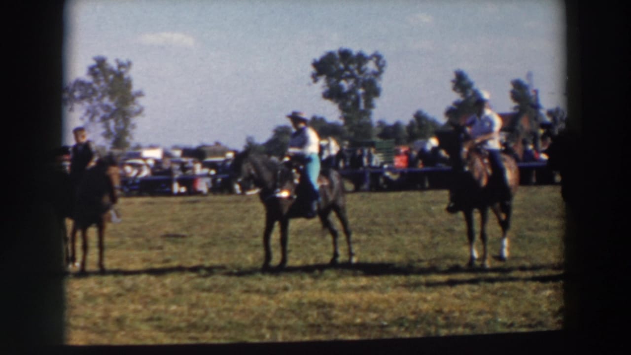 1957 Wheeling, Ohio home-movie frame showing several riders on horseback waiting in a grassy equestrian field.