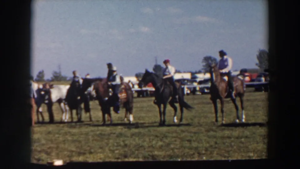Home-movie frame of riders and horses spread across a grass field during a 1957 horse event in Wheeling, Ohio.