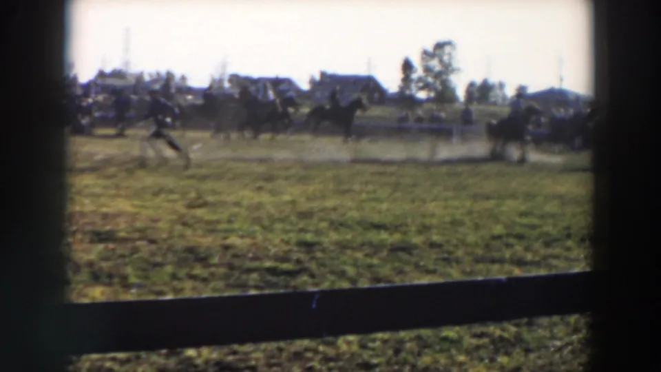 1957 Wheeling, Ohio home-movie frame showing riders on horseback moving across a grassy competition field.