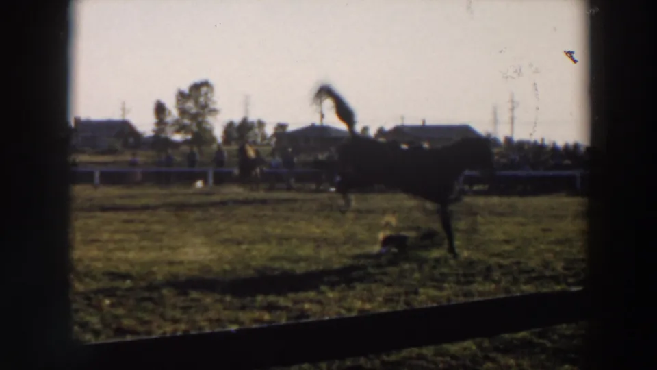 1957 Wheeling, Ohio frame with the bronco rearing while a rider appears to be thrown or down near the horse on the rodeo field.