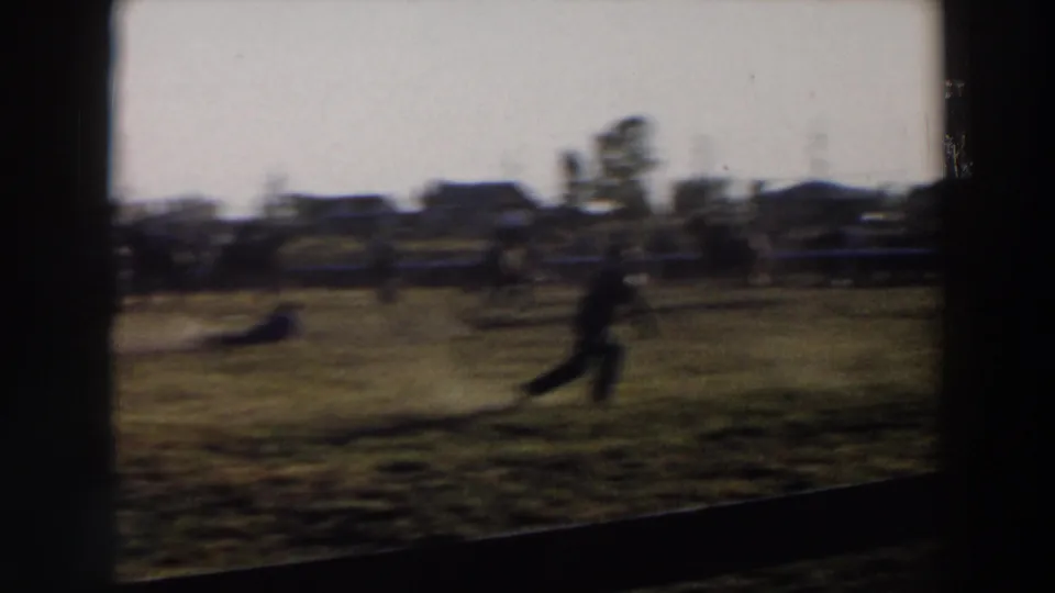 A soft 1957 Wheeling, Ohio rodeo frame shows a blurred person crossing the grassy field with spectators and fencing in the background.