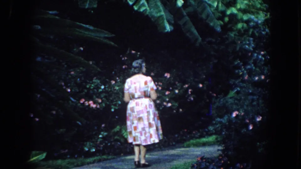 Near the end of the clip, the woman stands farther down the garden path under large tropical leaves in the supplied Florida setting.