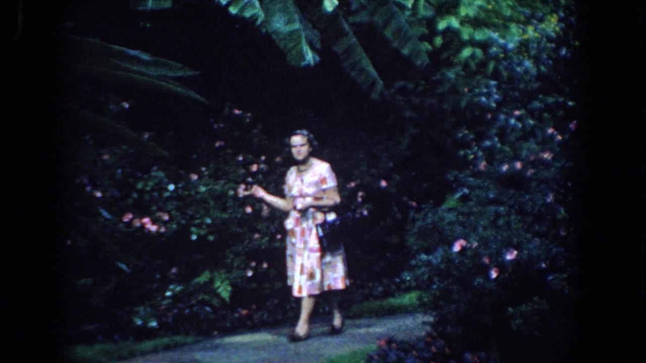 Woman gesturing toward plants while standing beside a garden path.