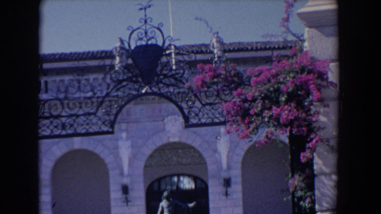 Ornate arched building entrance with statue and pink bougainvillea.